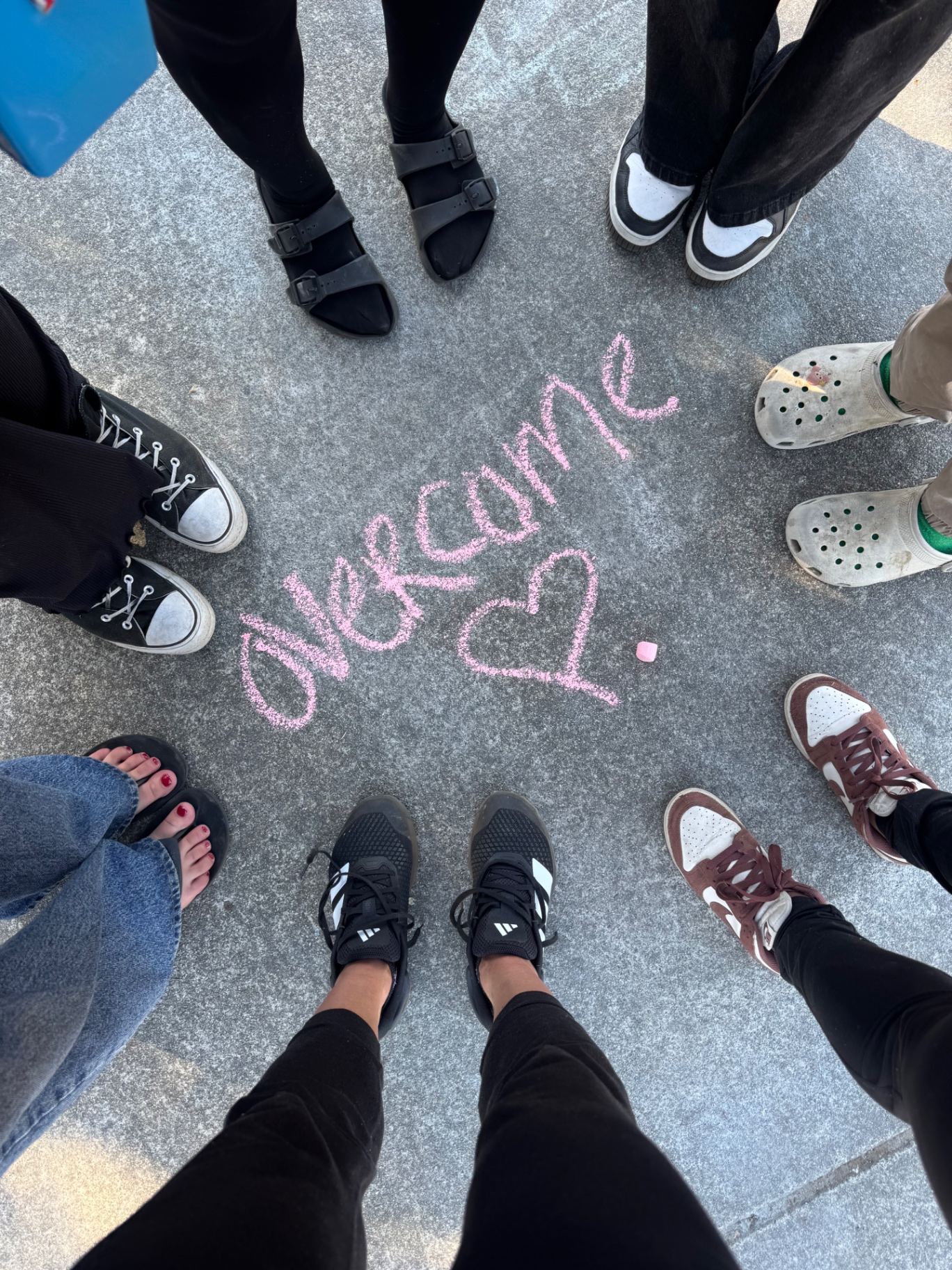 A circle of people around the word overcome written in pink chalk