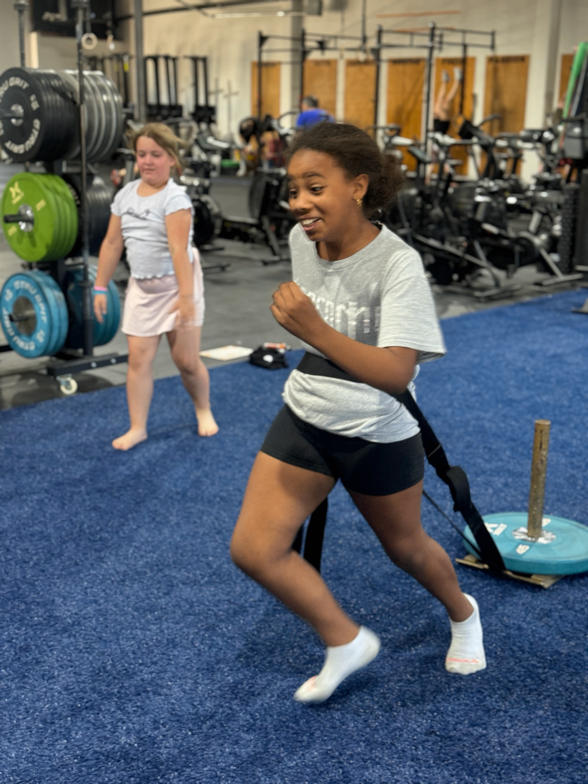 A young athlete pulling a weighted sled on blue gym turf